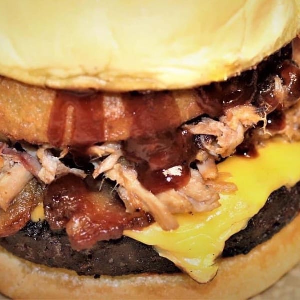 Close-up of a Doc's Smokehouse burger with pulled pork, melted cheese, and BBQ sauce.