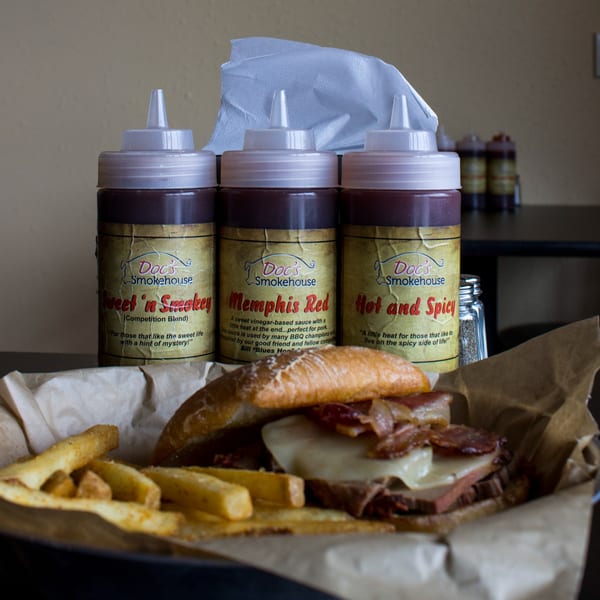 Doc's Smokehouse BBQ sandwich with fries and three squeeze bottles of barbecue sauce.