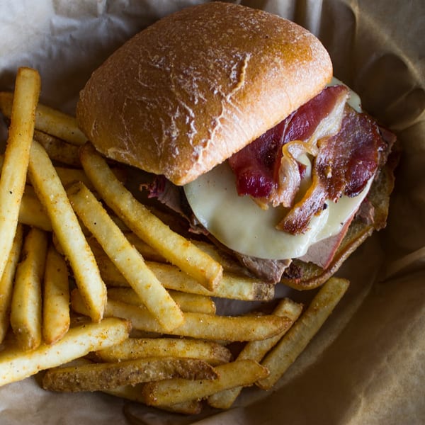 Doc's Smokehouse BBQ sandwich with bacon, cheese, and fries in a paper-lined basket.