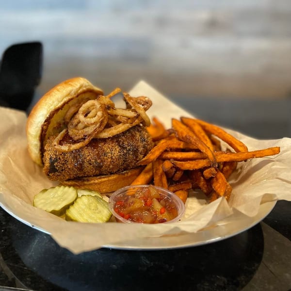 Doc's Smokehouse BBQ sandwich with crispy onions, sweet potato fries, pickles, and relish.