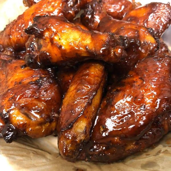 Close-up of Doc's Smokehouse BBQ chicken wings, glistening with dark, rich sauce.